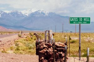 In der Alvord-Wüste (Alvord Desert) im US-Bundesstaat Oregon steht an einer Landstraße ein Schild mit der Aufschrift "Gates to hell - not a public road" ("Pforten zur Hölle - keine öffentliche Straße"). Im Hintergrund sind schneebedeckte Berge zu sehen.