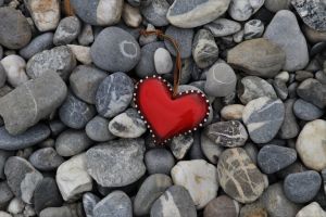 Ein rotes Herz mit einer Schnur liegt auf Steinen. Das Leuchten der Farbe hebt das Herz vom Hintergrund ab.