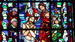 Ein Glasfenster zeigt Johannes den Täufer, der Jesus im Jordan tauft. Das Bild zeigt außerdem zwei Zuschauer.