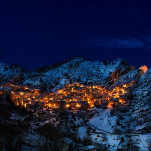 Das süditalienische Bergdorf Castelmezzano leuchtet in einer winterlichen Nacht. Der Ort liegt in den Lukanischen Dolomiten, die auf dem Bild mit Schnee bedeckt zu sehen sind.