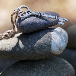Ein silberner Schlüssel mit Schnur zum Befestigen liegt auf einem Stapel Steine in der Sonne. Das Bild symbolisiert Ruhe, Harmonie, Gleichgewicht beziehungsweise Balance.
